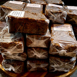 Stacks of raw African black soap wrapped in plastic on a wooden surface.