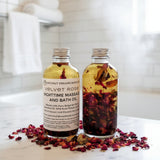 Two bottles of Coconut Dreams Skincare Velvet Rose Nighttime Massage and Bath Oil with rose petals on a wooden surface.