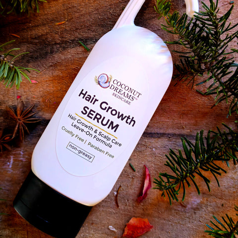 Coconut Dreams Skincare hair serum bottle on wooden surface with evergreen branches.